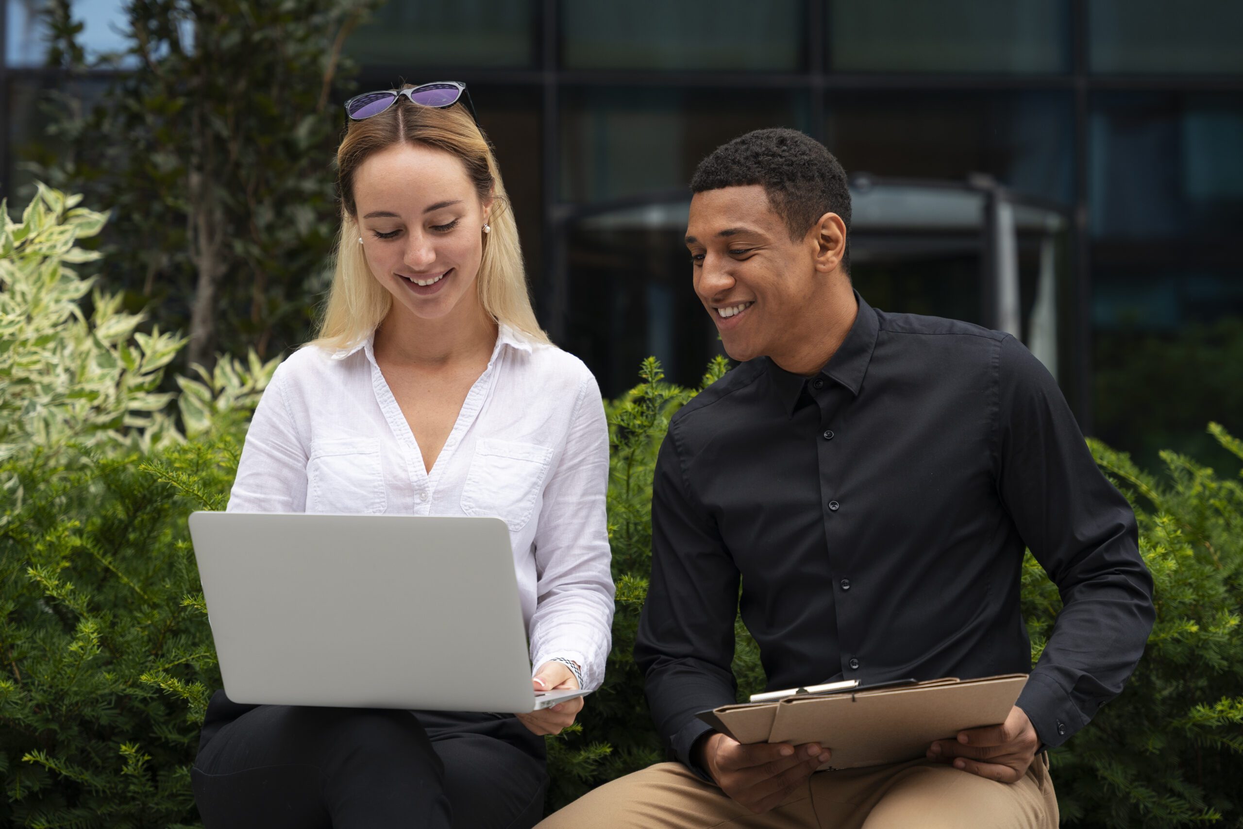 a man and woman sitting outside looking at a laptop